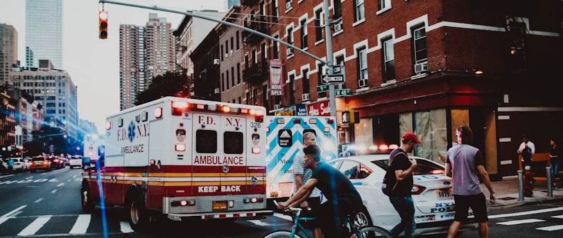 three people walking near man riding bicycle on street near ambulance