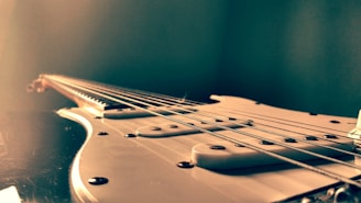 A close-up of a vintage electric guitar with worn wood and metal strings, set against a dark, moody background.
