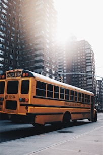 A bright yellow school bus parked in front of a school building on a sunny day.
