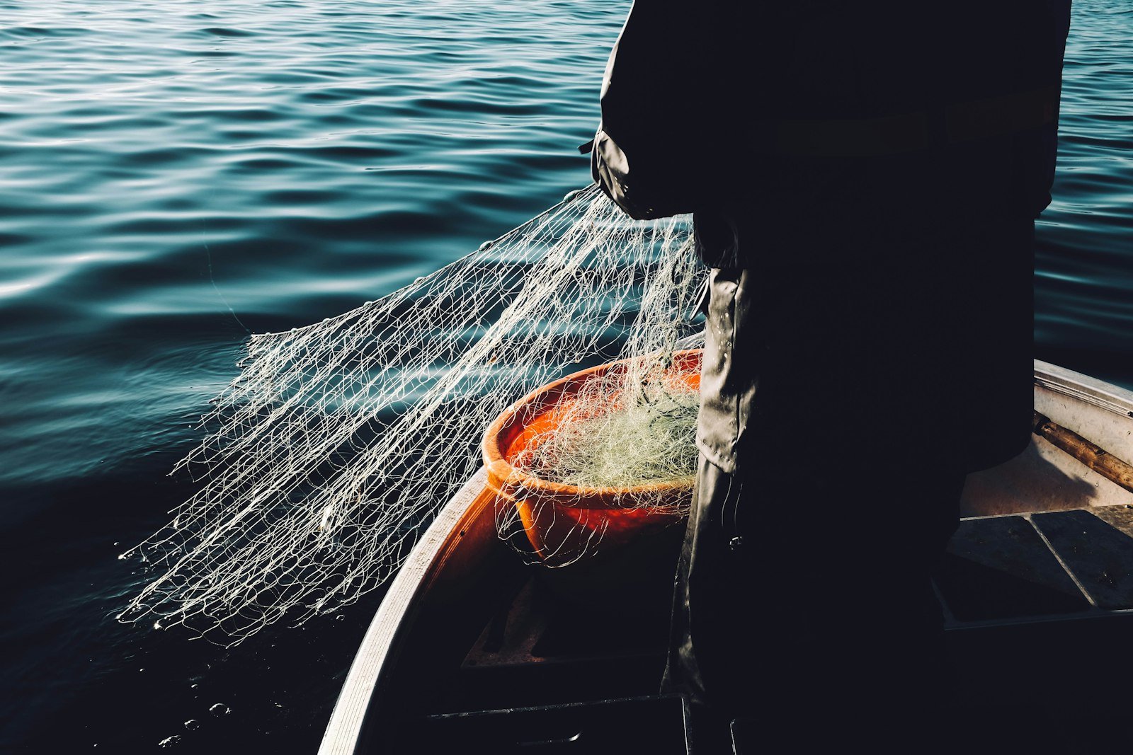 A commercial fisherman in foul weather gear handling a net on the deck of a working boat.