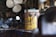 A weathered and rusty paint can sits on a workbench in a cluttered workshop. The label on the can is partially visible and reads 'EXTERIOR.' The background is blurred, highlighting shelves filled with various tools and equipment. A large industrial fan is visible in the background.