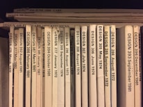 A collection of design journals is shelved vertically, with each journal's spine displaying the title 'DESIGN' followed by issue numbers and publication dates in chronological order from 1972 to 1986. The spines are mostly white or beige, with black print, and arranged with some minor wear visible on a few.