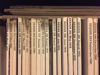 A collection of design journals is shelved vertically, with each journal's spine displaying the title 'DESIGN' followed by issue numbers and publication dates in chronological order from 1972 to 1986. The spines are mostly white or beige, with black print, and arranged with some minor wear visible on a few.