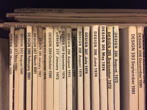 A collection of design journals is shelved vertically, with each journal's spine displaying the title 'DESIGN' followed by issue numbers and publication dates in chronological order from 1972 to 1986. The spines are mostly white or beige, with black print, and arranged with some minor wear visible on a few.