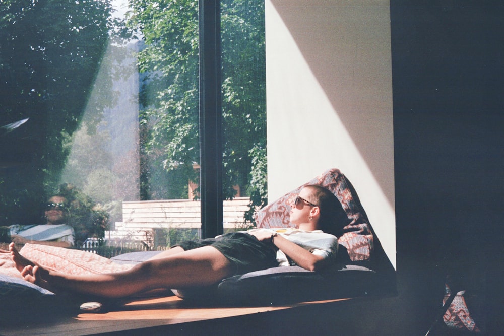 man lying on cushion beside glass window