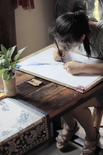 An artist sketching quietly in a sunlit studio surrounded by plants.