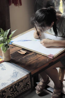 A person peacefully sketching in a sunlit room surrounded by plants.