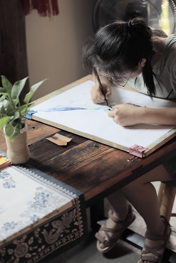 A focused student sketching geometric shapes on paper in a bright, organized study space.