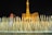 A nighttime scene featuring a dazzling fountain show with water jets elegantly arching in front of a replica Eiffel Tower and surrounding hotels. Bright lights illuminate the structure, contrasting against the dark evening sky.