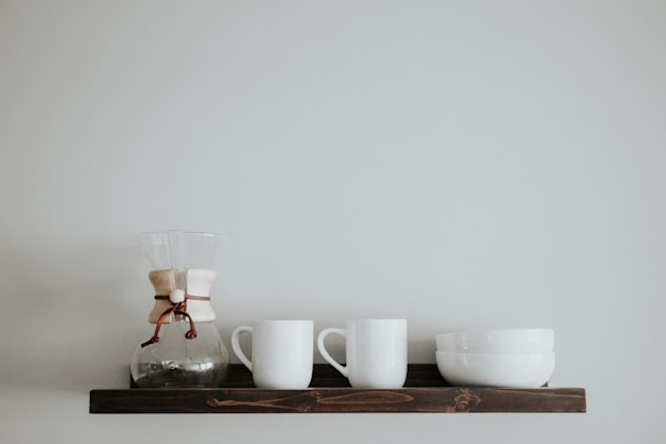Minimalist ceramic mugs arranged neatly on a light wooden shelf against a soft white wall
