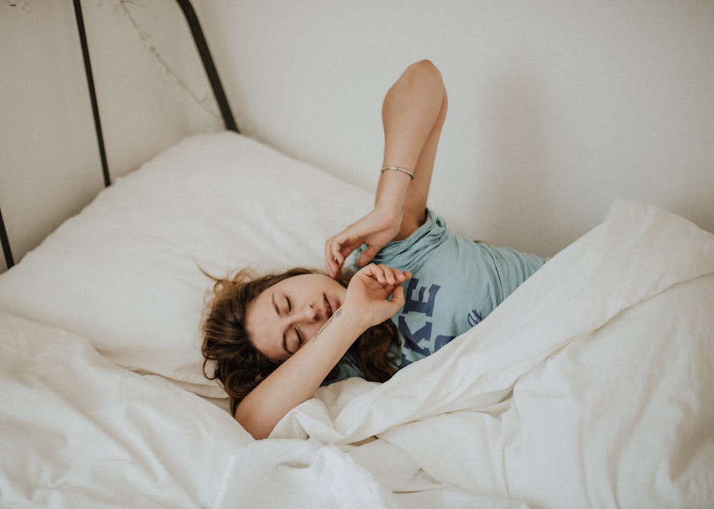 femme couverte d’une couverture blanche dormant sur une couette de lit blanc