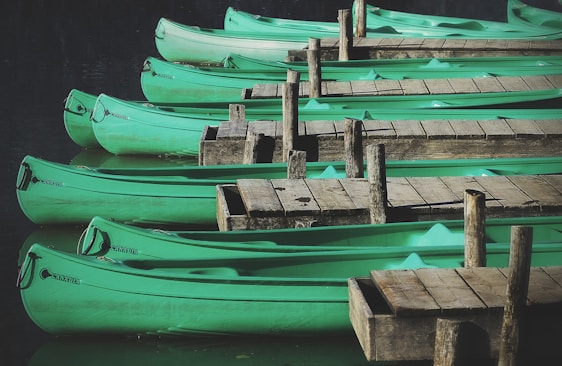 Several green canoes are aligned next to wooden docks on a calm body of water, reflecting a serene and organized setting. The canoes are in pristine condition and appear ready for use.