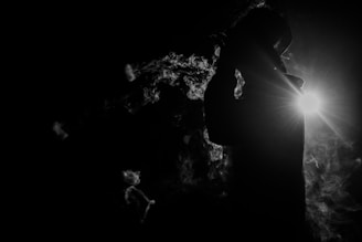 Silhouette of Saint Amari against a charcoal backdrop with subtle smoke.