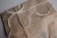 A brown paper package tied with a thin, rough twine. The twine is wrapped securely around the package and tied in a simple bow. The package is made of a rustic, textured brown paper and has a slightly uneven edge. There is a handwritten script visible on the surface of the package.