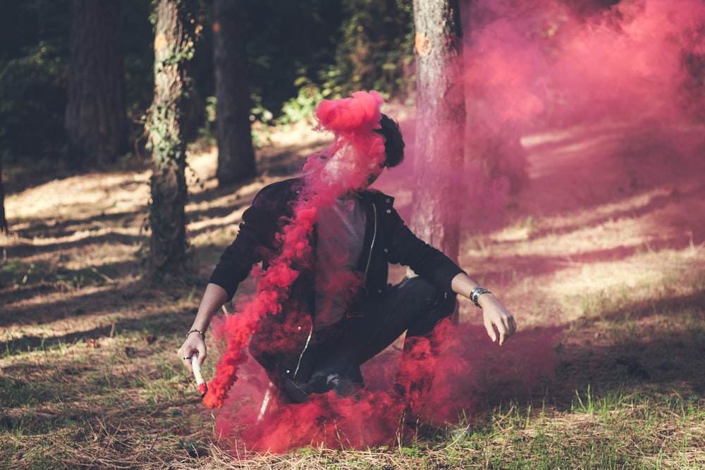 man wearing black jacket while sitting beside brown tree during daytime