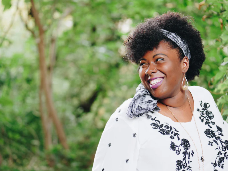 A woman with a patterned headwrap laughing outside in natural light.