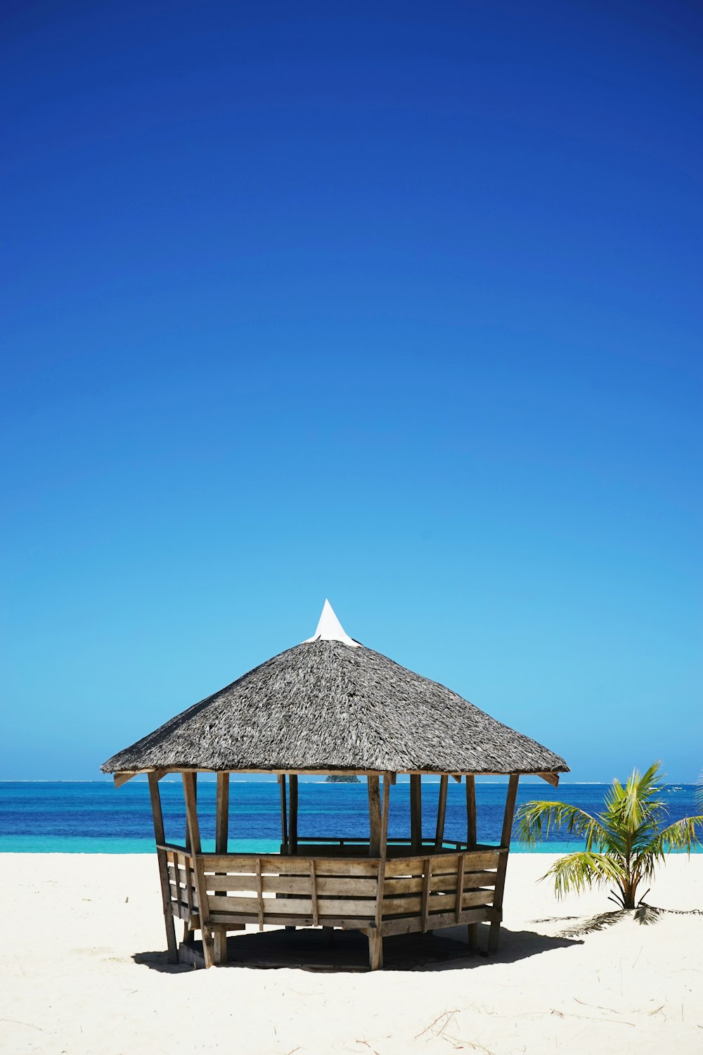 brown wooden nipa hut on white sand near body of water