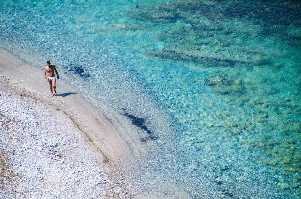 man walking on seashore beside blue se