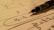 A mechanical pencil rests on a notebook filled with handwritten mathematical equations. The formulas include terms such as V3, V2 with elements circled and lines drawn across the page. The use of pen and paper suggests an academic or study setting.