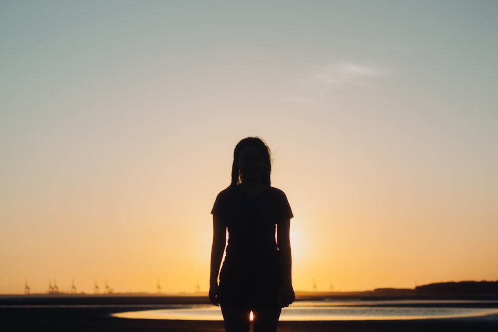silhouette photography of woman standing in front of body of water