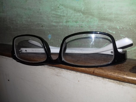 A stylish pair of eyeglasses resting on a wooden table surrounded by greenery.