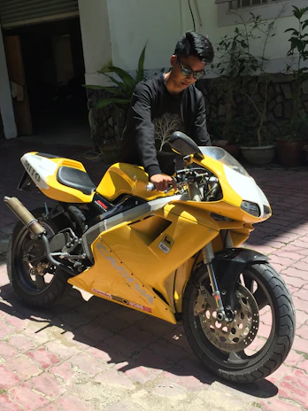 Rider wearing custom-sized gloves and boots, standing next to a sport motorcycle under bright sunlight.