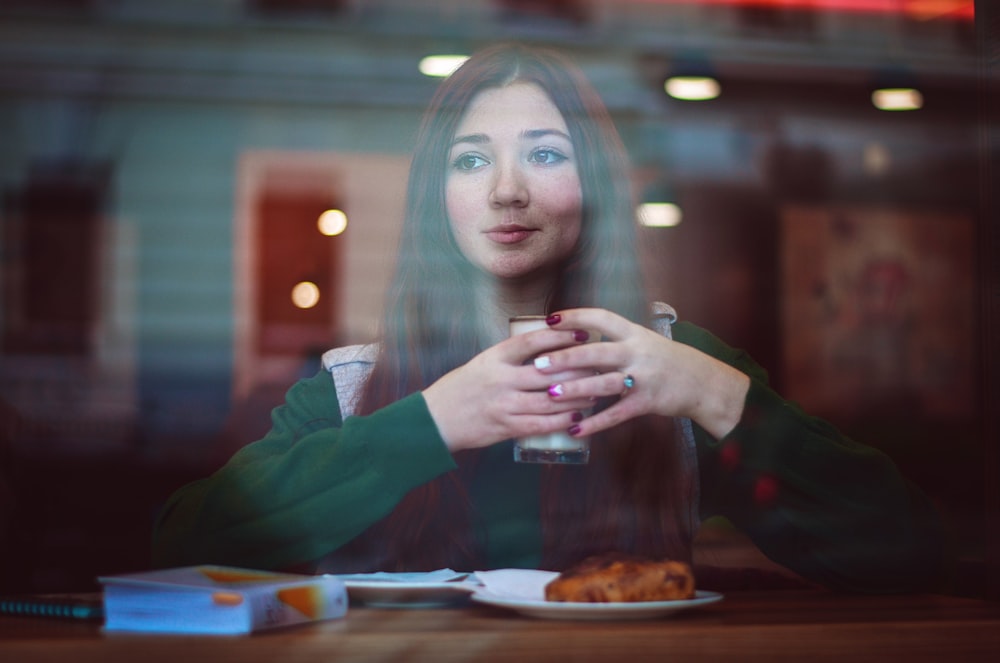 woman in green sweater sitting in front of table holding drinking glass