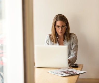 woman wearing grey striped dress shirt sitting down near brown wooden table in front of white laptop computer