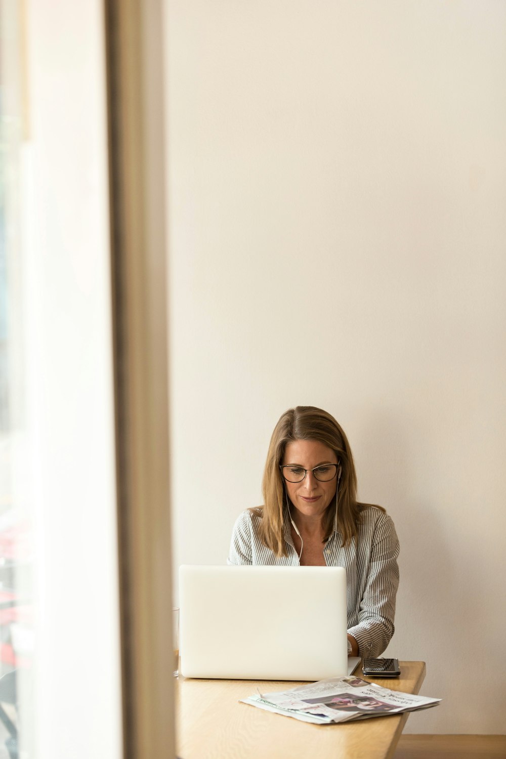 woman wearing grey striped dress shirt sitting down near brown wooden table in front of white laptop computer