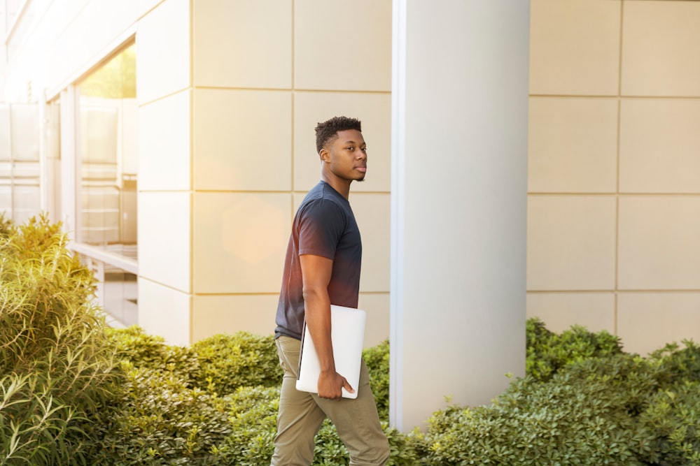 man holding laptop walking towards building