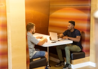 man sitting on black leather bench holding gray laptop computer on top of white wooden table