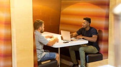 man sitting on black leather bench holding gray laptop computer on top of white wooden table