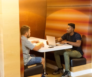 man sitting on black leather bench holding gray laptop computer on top of white wooden table