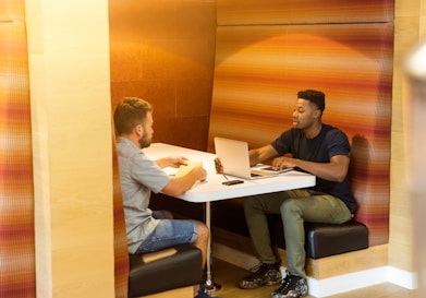 man sitting on black leather bench holding gray laptop computer on top of white wooden table