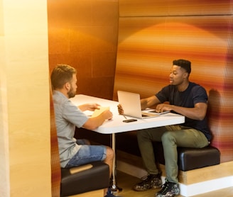 man sitting on black leather bench holding gray laptop computer on top of white wooden table