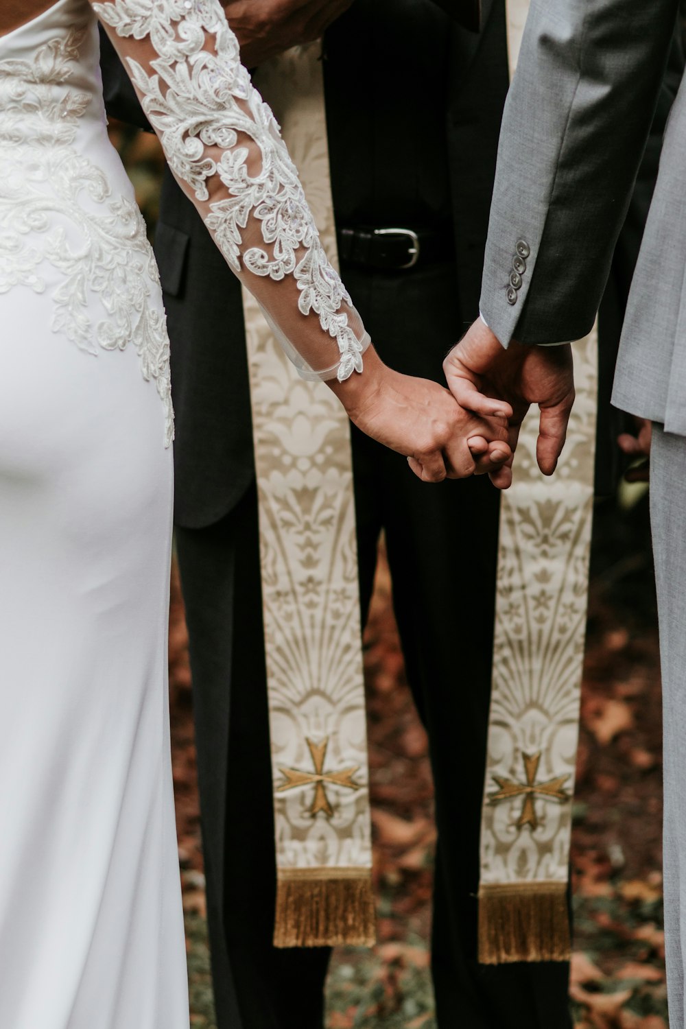 man and woman holding hands in front of priest during daytime