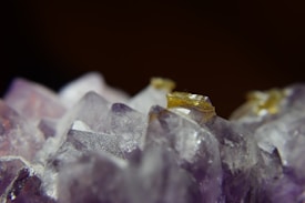 A close-up view of amethyst crystals with sharp edges and a mix of purple and golden colors. The background is dark, providing strong contrast to the vibrant and translucent nature of the crystals.