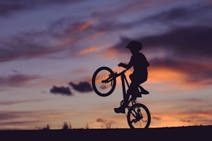 silhouette of boy riding bicycle in wheelie during golden hour