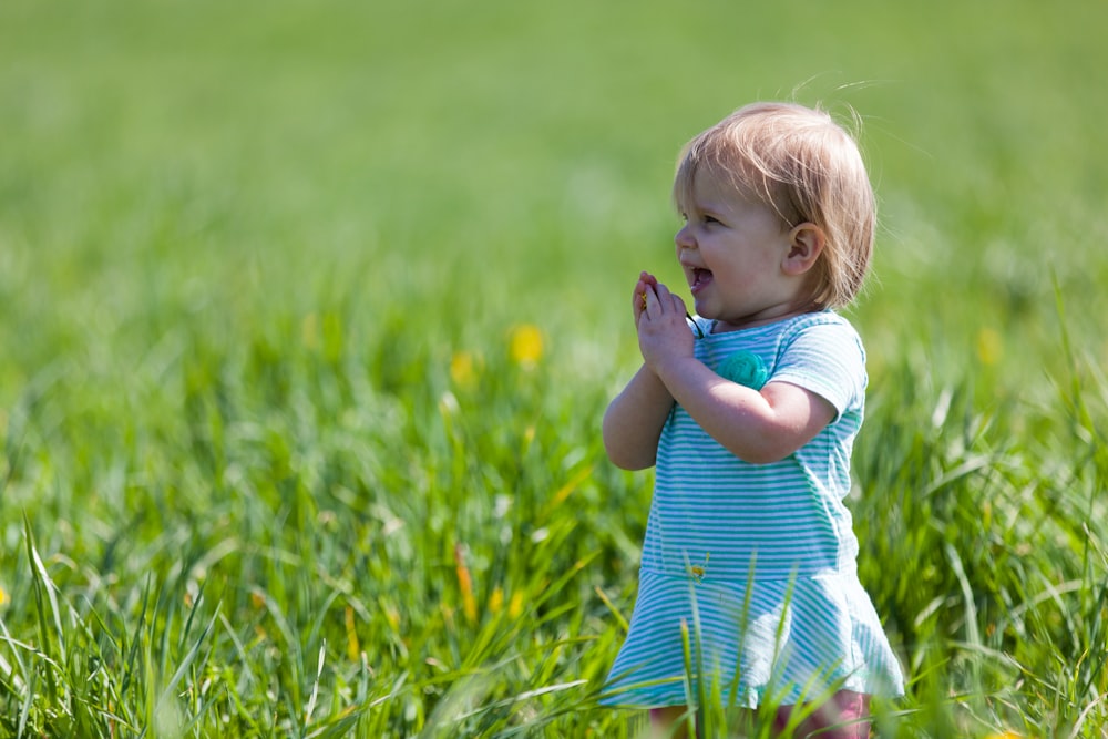 昼間の緑の芝生の上で青緑色のドレスを着た幼児