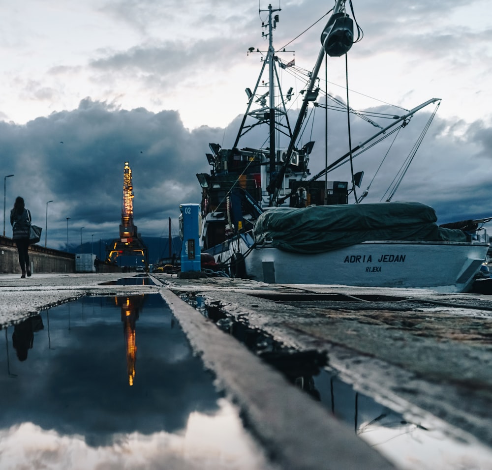 woman walking on pathway beside parked ship under white and blue cloudy skies