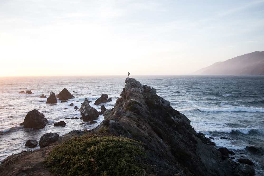 person standing on rock cliff near body of water