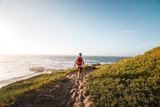 man walking while carrying red backpack near sea at daytime in Montana De Oro State Park United States