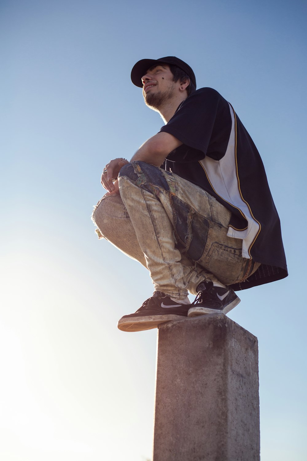 man in black and white jacket and brown pants sitting on brown concrete statue during daytime