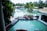 A luxurious resort setting with a large, inviting swimming pool surrounded by palm trees. There is a wooden deck area with dining tables and chairs arranged in a neat fashion. The atmosphere is serene and tropical, with the pool reflecting the greenery of the surrounding trees.
