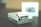 A small retro gaming console designed to resemble an old school entertainment system, featuring multiple USB ports on its front. The console is primarily white with some gray accents, and it sits on a dark surface. A blurred box with an image of the console is visible in the background.