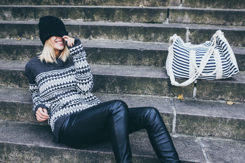 woman wearing gray and black tribal sweater and black pants sitting on gray concrete stair