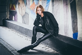 An edgy leather jacket paired with a graphic tee and slim black pants, posed against a graffiti wall.
