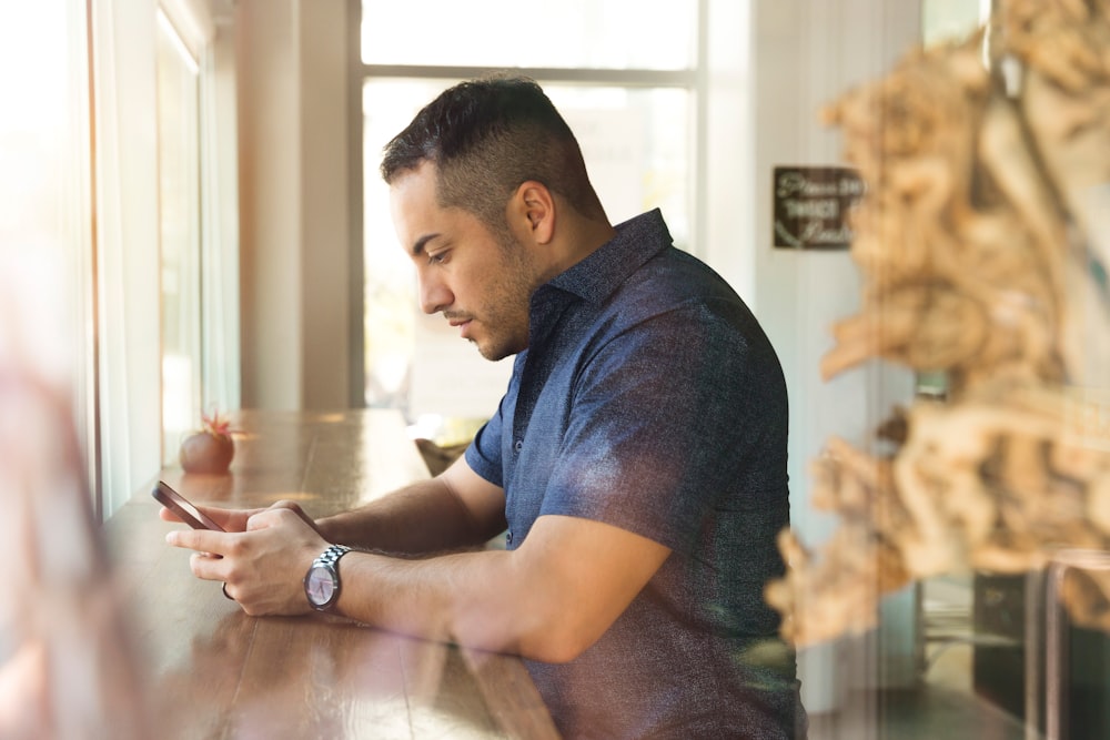 Mann im schwarzen Hemd mit Knopfleiste und Smartphone in der Hand