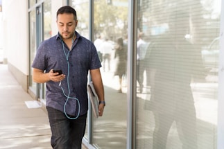man in blue button-down shirt walking beside glass wall during dayhtime