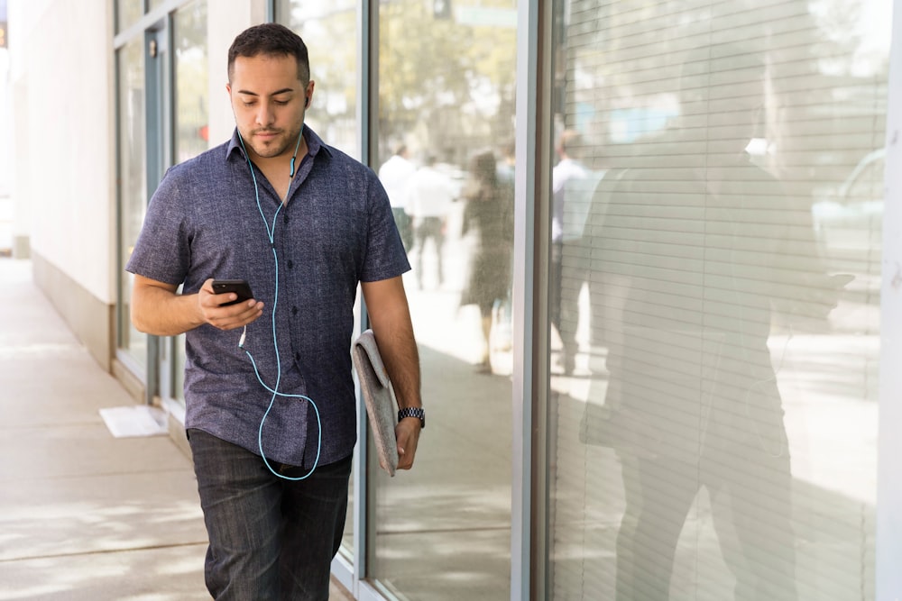 man in blue button-down shirt walking beside glass wall during dayhtime